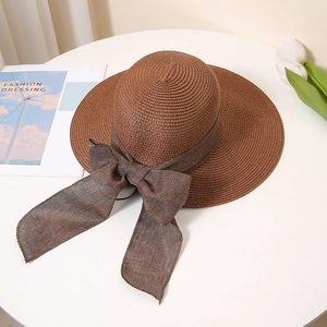 Detailed texture of brown straw sun hat with large bow on white pedestal