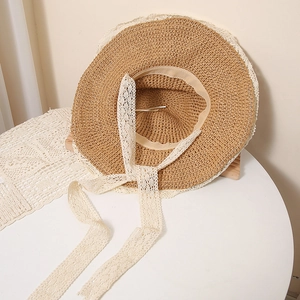 Detail view of woven straw hat featuring white lace trim and adjustable lace tie straps