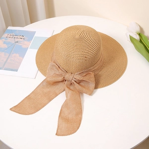 Close-up of khaki straw sun hat with large bow detail on a white table with tulips