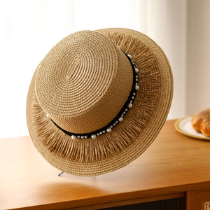 Dettaglio cappello di paglia con nastro di perle e tesa con frange a nappe
