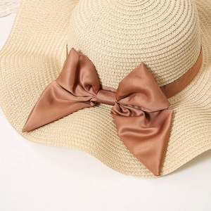 Close-up of wide brim straw hat featuring a large brown satin bow and dense weaving texture