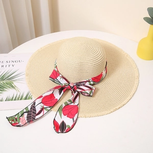 Close-up of beige woven straw hat with floral print ribbon bow and frayed edge detail
