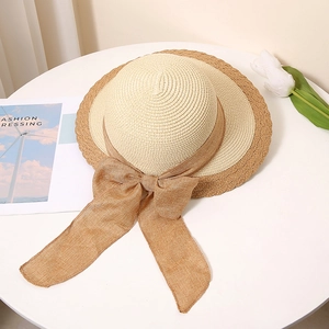 Detail of color-block straw hat with large bow on white table with white tulips