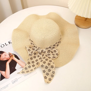 Detail of a beige woven straw sun hat featuring a wave brim and floral ribbon bow decoration