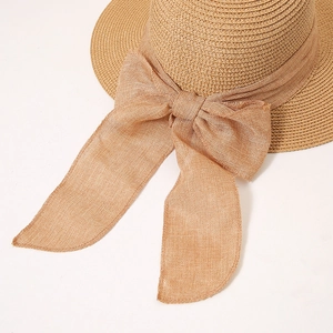 Close-up of hand-woven straw hat texture featuring a large decorative bow and linen ribbon