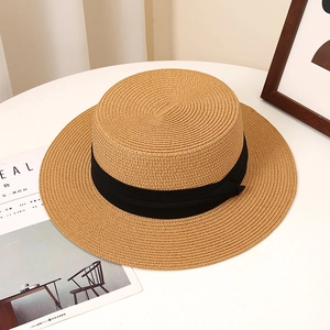 Close-up of a natural straw boater hat with a black ribbon on a minimalist white desk