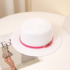 Chapeau de paille à haut plat pour femme avec ruban rose et boucle dorée sur table blanche