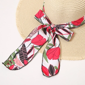 Close-up of straw sun hat featuring a floral ribbon bow and frayed fringe brim edge