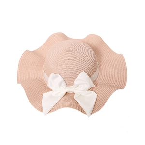 Pink straw sun hat with wavy brim and white satin bow for beach vacation fashion