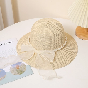 Détail d'un chapeau de paille beige avec un nœud en mousseline perlé sur une table