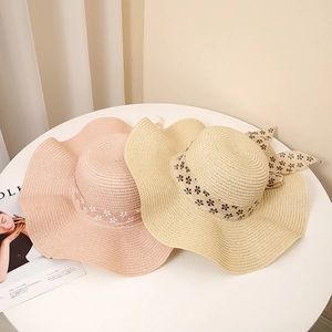 Summer straw sun hats with wavy brim and floral bow ribbon on white table