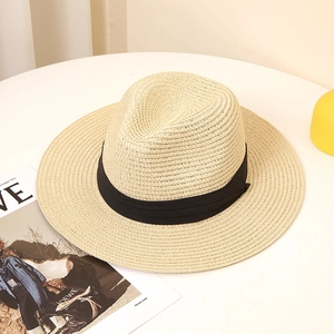 Top view of a breathable straw fedora hat with a black ribbon on a minimalist white desk