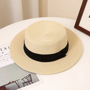 Detail of light beige boater hat with black ribbon on a white table next to cereal magazine