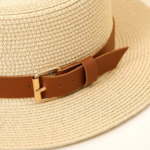 Macro detail of beige boater hat showing fine straw weave and brown leather strap with buckle