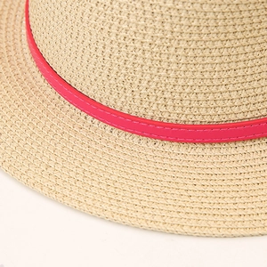 Détail du chapeau de paille plat avec tissage dense et ruban décoratif en cuir rose vif