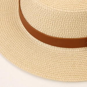 Detail of light beige straw hat featuring fine weave texture and brown leather decorative band