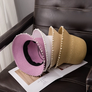Straw sun hats with pearl trim in pink, white and khaki displayed on a leather chair