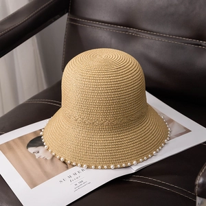 Close-up of a straw bucket hat with pearl trim detail resting on a magazine and leather seat