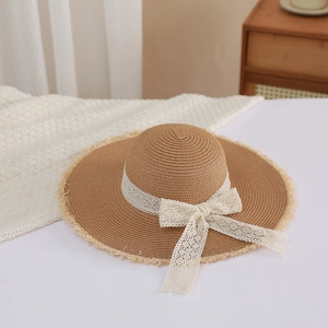 Detailed close-up of straw sun hat with frayed brim and elegant white lace bow decoration