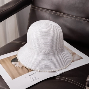 Detail view of a white straw sun hat with elegant pearl trim on a leather chair