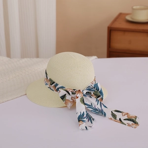 Detail of light beige woven straw hat featuring an orange floral ribbon bow accent