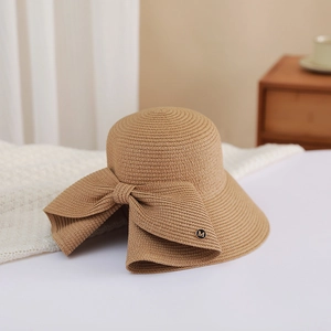 Close-up of the light brown woven straw hat featuring a large bow and M-letter metal badge