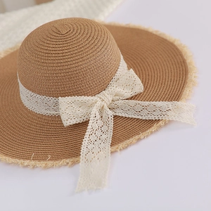 Close-up of woven straw hat featuring a lace ribbon bow and frayed fringe edge detail