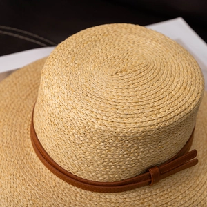 Detail view of woven straw sun hat featuring flat top and brown leather strap accent