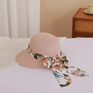 Close-up of light pink woven straw hat with floral ribbon bow and wide brim detail