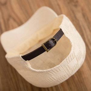 Detail of cream knit baseball cap with brown leather strap and brass buckle closure