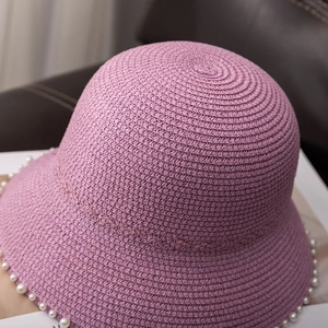 Detail of purple straw sun hat featuring woven texture and white pearl trim on the brim