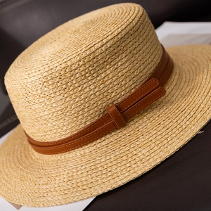 Detail of a natural boater straw hat featuring a brown faux leather double strap and buckle