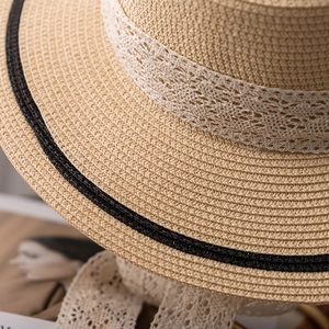 Gros plan d'un chapeau en paille beige avec dentelle florale blanche et rayures noires