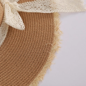 Detailed close-up of straw sun hat featuring lace bow and frayed fringe edges