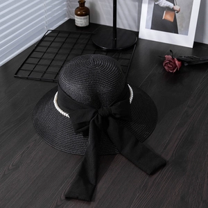 Detail of elegant black straw hat featuring a bow and pearl beads on a wooden desk