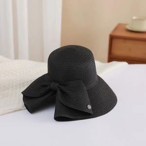 Detail of black straw sun hat with large bow and silver M logo on a white bed
