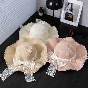 Three elegant summer straw sun hats with lace bows and scalloped brims on wood