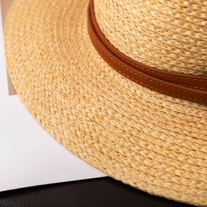 Close-up detail of fine straw weave and brown leather band with decorative stitching