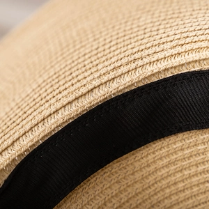Détail du tissage dense en paille naturelle et du ruban noir élégant sur le chapeau d'été