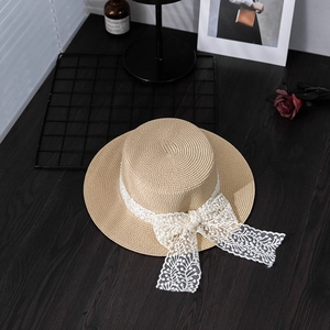 Summer straw boater hat with white lace bow on a vintage wood background