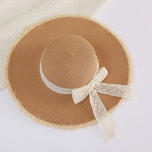 Top view of woven straw sun hat with white lace bow and raw fringe edges on white background