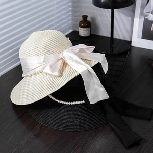 Elegant straw sun hat with large bow and pearl trim shown on a rustic wooden desk