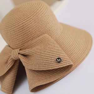 Detailed macro view of woven straw sun hat with decorative ribbon and metallic M emblem