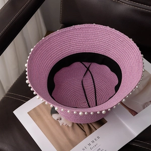 Detail of pink woven straw hat featuring elegant white pearl trim and adjustable inner strap
