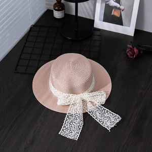 Detailed top view of a pink boater straw hat with white lace ribbon on a wooden desk