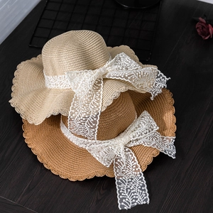 Summer straw sun hat with wide wavy brim and large white lace bow decoration