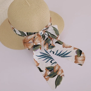 Close-up of beige woven sun hat with floral silk ribbon and large bow detail
