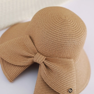 Detailed macro view of woven straw hat featuring a chic bow and metallic M logo emblem