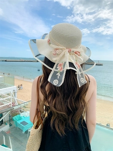 Detail of wide brim straw sun hat featuring a white lace bow and pink rose embroidery