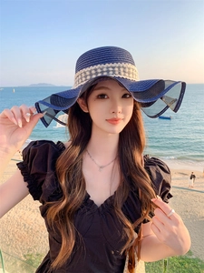 Dettaglio del cappello di paglia blu navy con nastro in pizzo e tesa ondulata a rete